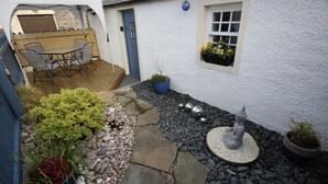 A small cottage with a patio, a dining table, and various potted plants. - Zen Cottage, Cullen - Sleeps 4, Garden & Pets Ok (Buckie)