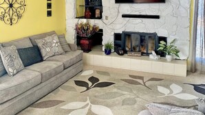 A living room with a sofa, a flat-screen TV mounted on a stone wall, a fireplace, and a decorative wall piece. - Unique Home Near Temple and Parks, great for families! (Pocatello)
