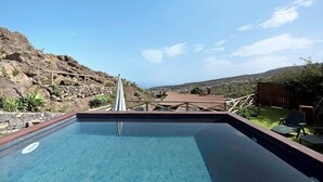 Une piscine entourée d’une terrasse en bois, d’une clôture en bois, et offrant une vue sur un paysage vallonné.