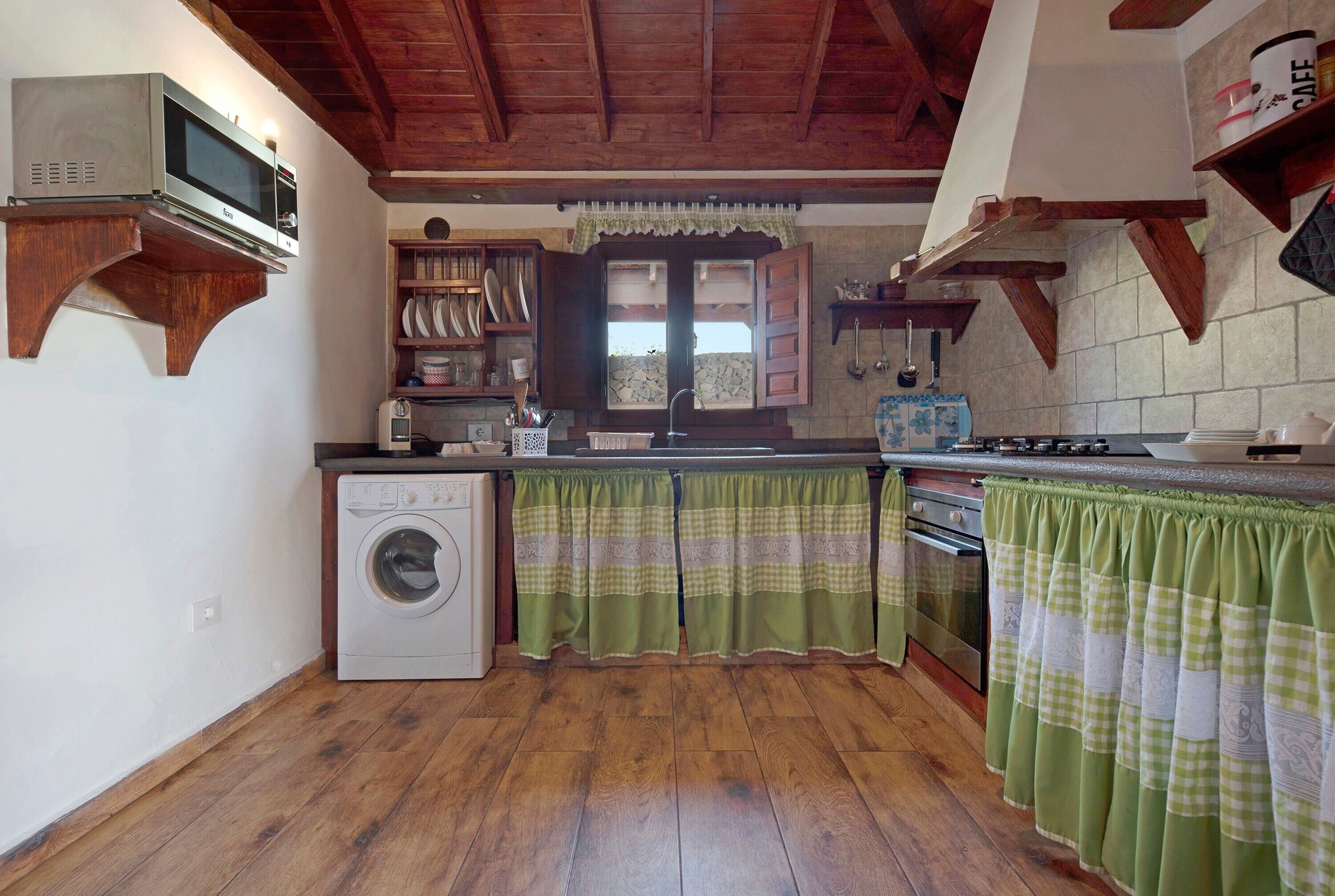 A kitchen with wooden beams, a washing machine, a microwave, and a stove.