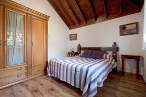 Een slaapkamer met een houten kledingkast, een bed met gestreept beddengoed, een nachtkastje en een klein tafeltje.