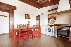 Une cuisine avec des chaises en bois, un lave-linge, un four et un tableau représentant des fruits accroché au mur.