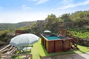 Un bain à remous en bois avec une piscine, entouré d’une terrasse en bois et agrémenté d’un parasol.