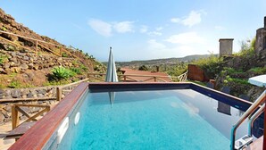 A swimming pool with a wooden deck and stone walls, surrounded by a stone wall and vegetation. - Vacation Home "Casa Rural Romance" with Sea View, Jacuzzi & Wi-Fi (Icod de los vinos)
