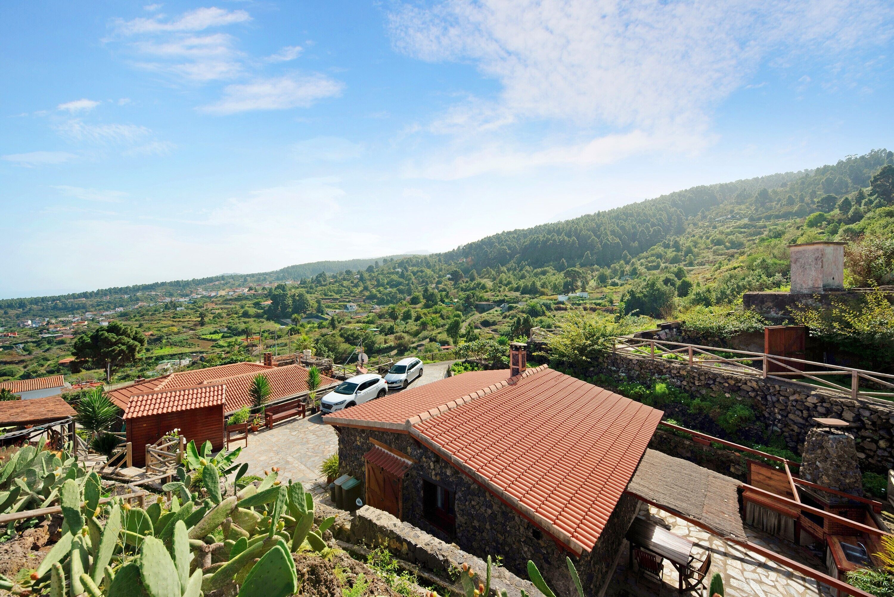 Un entorno rural con edificios de piedra, una zona pavimentada y vehículos.