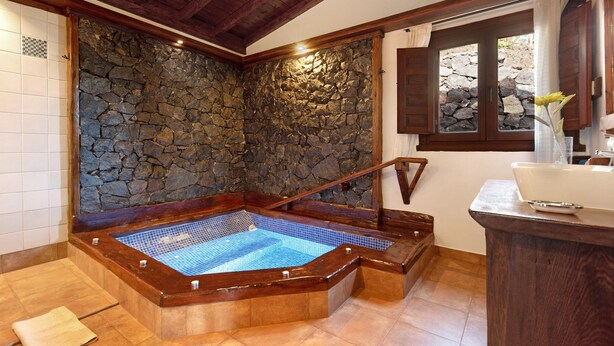 A spa area with a stone wall, wooden bathtub, and a window with curtains. - Vacation Home "Casa Rural Romance" with Sea View, Jacuzzi & Wi-Fi (Icod de los vinos)
