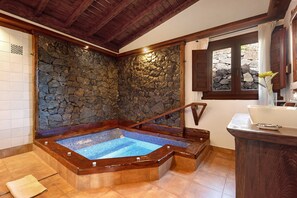 Un espace de détente avec un mur en pierre, une baignoire en bois et une fenêtre avec des rideaux.