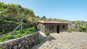 A stone house with a tiled roof, a stone wall, and a paved courtyard. - Vacation Home "Casa Rural Romance" with Sea View, Jacuzzi & Wi-Fi (Icod de los vinos)