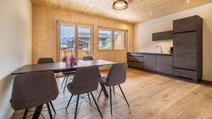 Moderni keittiö, jossa on puinen katto, ruokailutila pöytineen ja tuoleineen sekä näkymä talolle suurista ikkunoista.