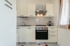 A compact kitchen with white cabinets, a stainless steel range hood, a built-in oven, and a coffee maker.