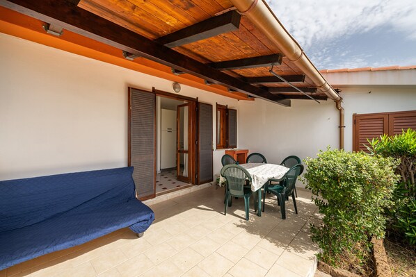 A covered patio with a table and chairs, a blue sofa, and a door leading to an interior space.