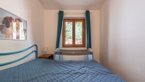 A bedroom with a bed, a window with curtains, a bedside table, and a wall-mounted picture. - Villa 'Villetta Teresa' with Sea View, Private Garden, Terrace & A/C (Costa Rei)