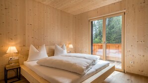 Une chambre à coucher aux murs lambrissés, avec un lit, deux lampes de chevet et une porte-fenêtre coulissante donnant sur une terrasse extérieure.