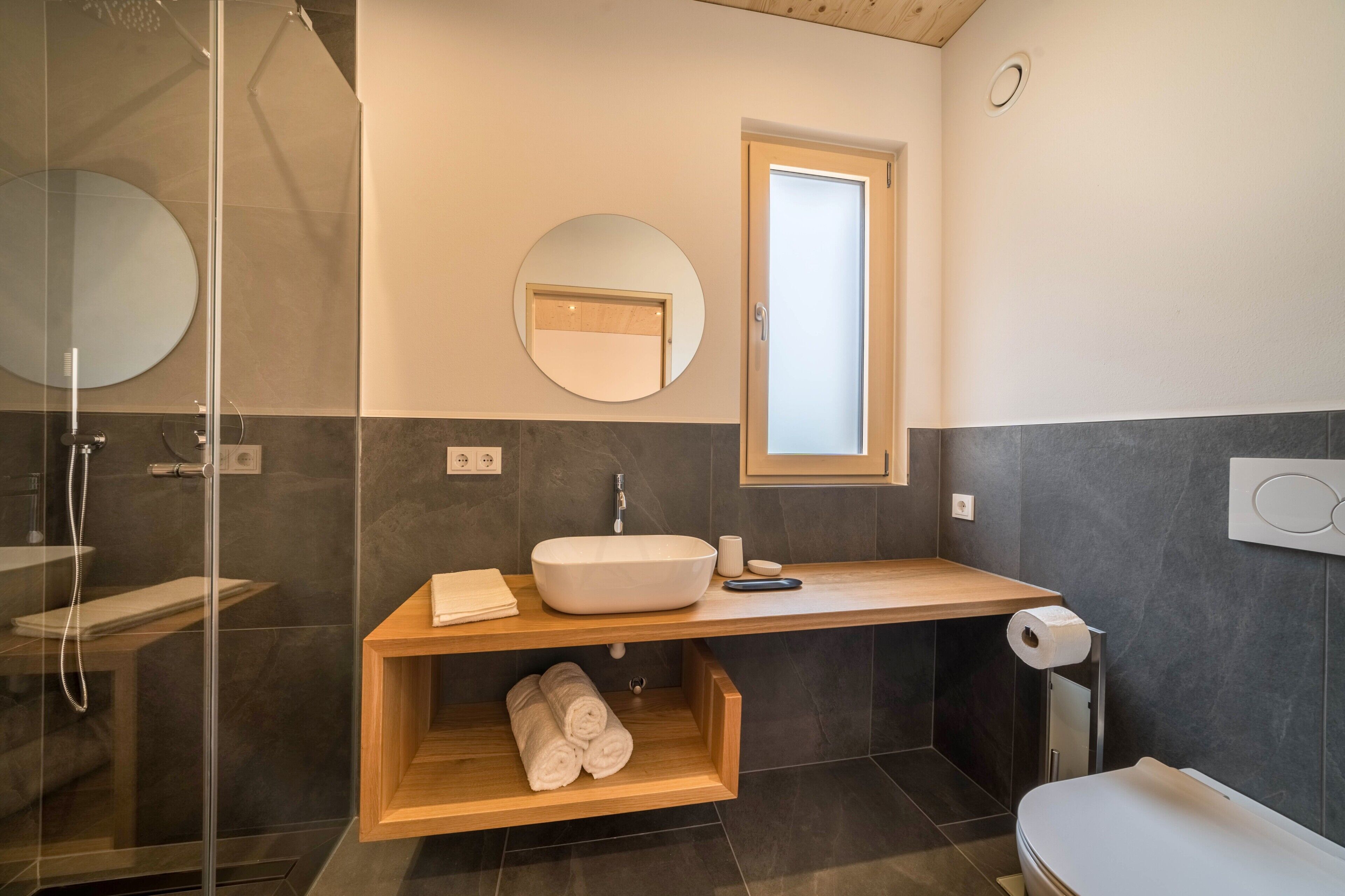 A modern bathroom with a glass-enclosed shower, a wooden vanity with a sink, and a toilet.