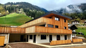 Un bâtiment moderne à deux étages, doté d’une façade en bois, d’un espace extérieur couvert et offrant une vue sur un paysage montagneux.
