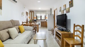 Ein Wohnzimmer mit Sofa, Couchtisch, Fernseher und einer Küche im Hintergrund.