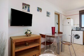 Une cuisine compacte comprenant un lave-linge, une table à manger avec des chaises, un téléviseur fixé au mur et une petite étagère avec des objets décoratifs.