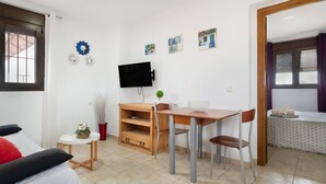 A room with a bed, a small table with chairs, a TV, and a window with curtains. - Holiday Apartment 'Villa Fornell Atico' with Shared Pool, Terrace and Wi-Fi (Conil)