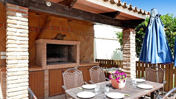 An outdoor patio with a brick oven, dining table, chairs, and a blue umbrella. - Holiday Apartment 'Villa Fornell Atico' with Shared Pool, Terrace and Wi-Fi (Conil)
