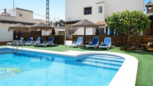 A swimming pool with lounge chairs, a wooden fence, and a tree with fruit. - Holiday Apartment 'Villa Fornell Atico' with Shared Pool, Terrace and Wi-Fi (Conil)