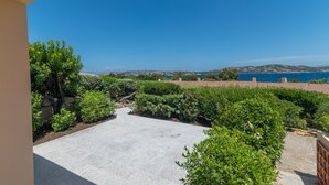 Un patio con suelo empedrado, rodeado de vegetación y vistas al mar.
