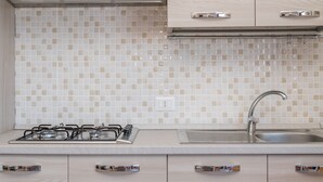Cozinha com fogão a gás, pia de aço inoxidável e painel de azulejos em tons claros.