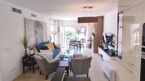 A modern living room with a sofa, chairs, a dining table, and a kitchen area with cabinets and a TV.