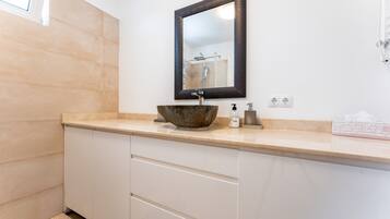 A bathroom with a beige countertop, a large mirror, a vessel sink, a soap dispenser, and a towel rack.