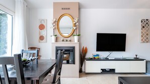A modern living room with a fireplace, a flat-screen TV, a dining area with chairs, and a large mirror.