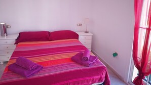 A bed with a striped bedspread, two pillows, a nightstand with a lamp, and a window with red curtains.