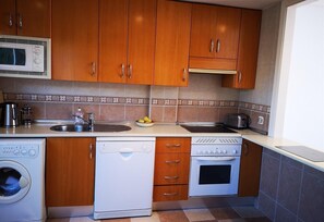 A compact kitchen with wooden cabinets, a microwave, a dishwasher, a stove, and a sink.