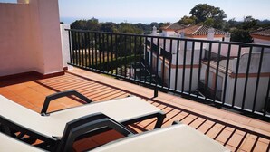 A balcony with a view of a residential area, a white chair, and a black metal railing.