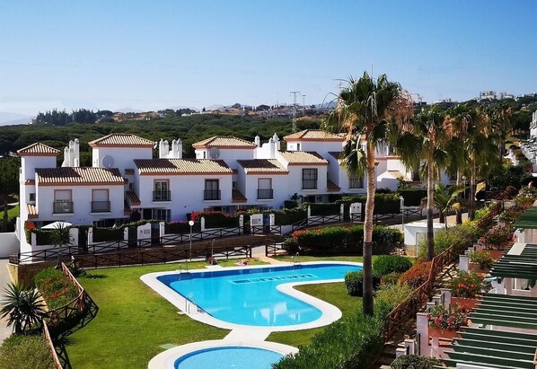 A resort with multiple white buildings, a swimming pool, and palm trees.