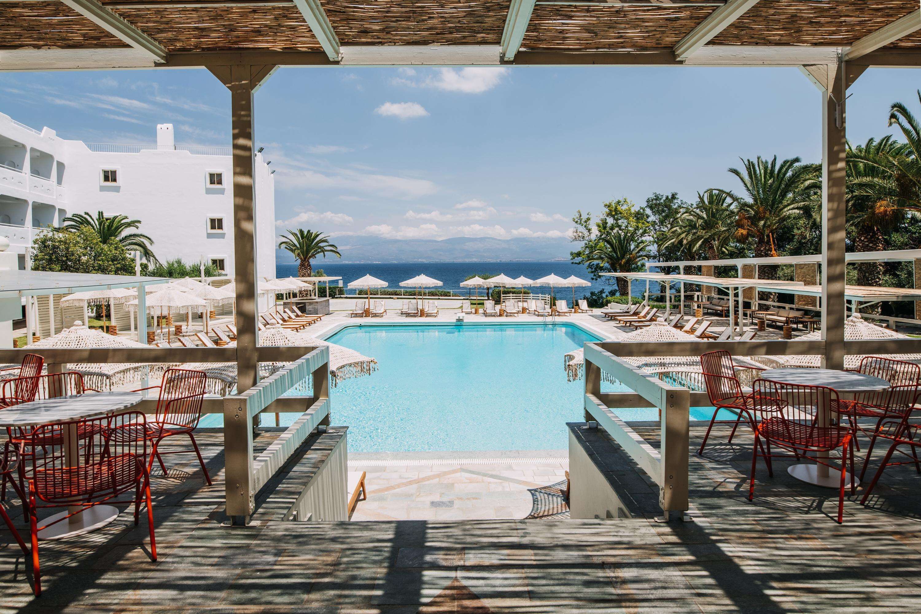 A pool area with sun loungers and umbrellas, overlooking a clear blue sea.