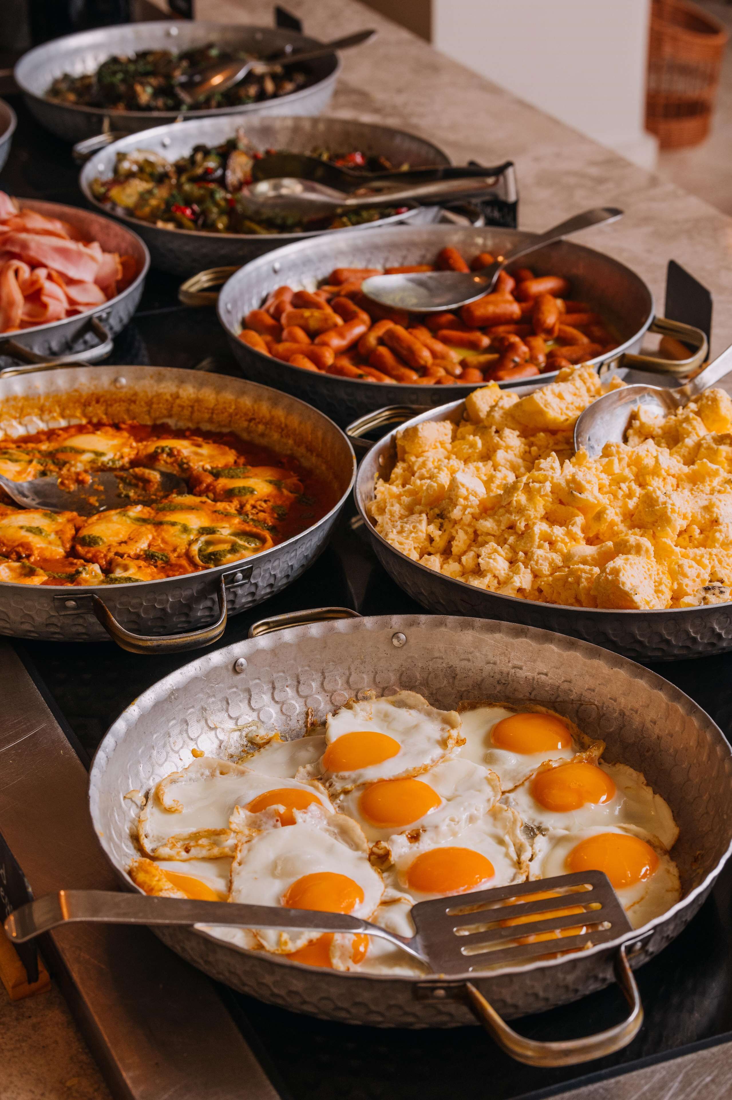 A variety of dishes including scrambled eggs, sausages, and vegetables on a buffet table.