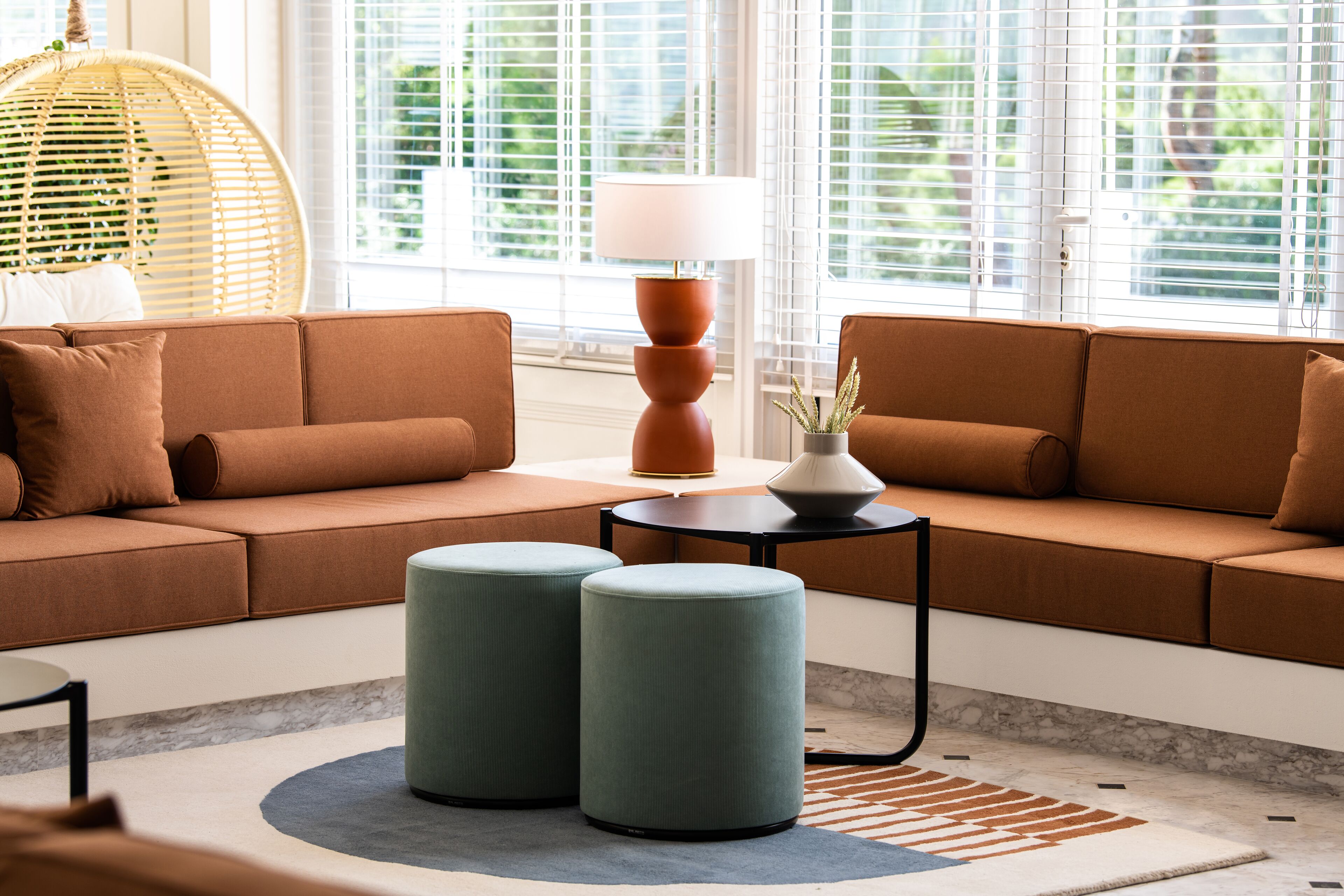 A modern living room with a brown sofa, two ottomans, a round table, and a lamp.