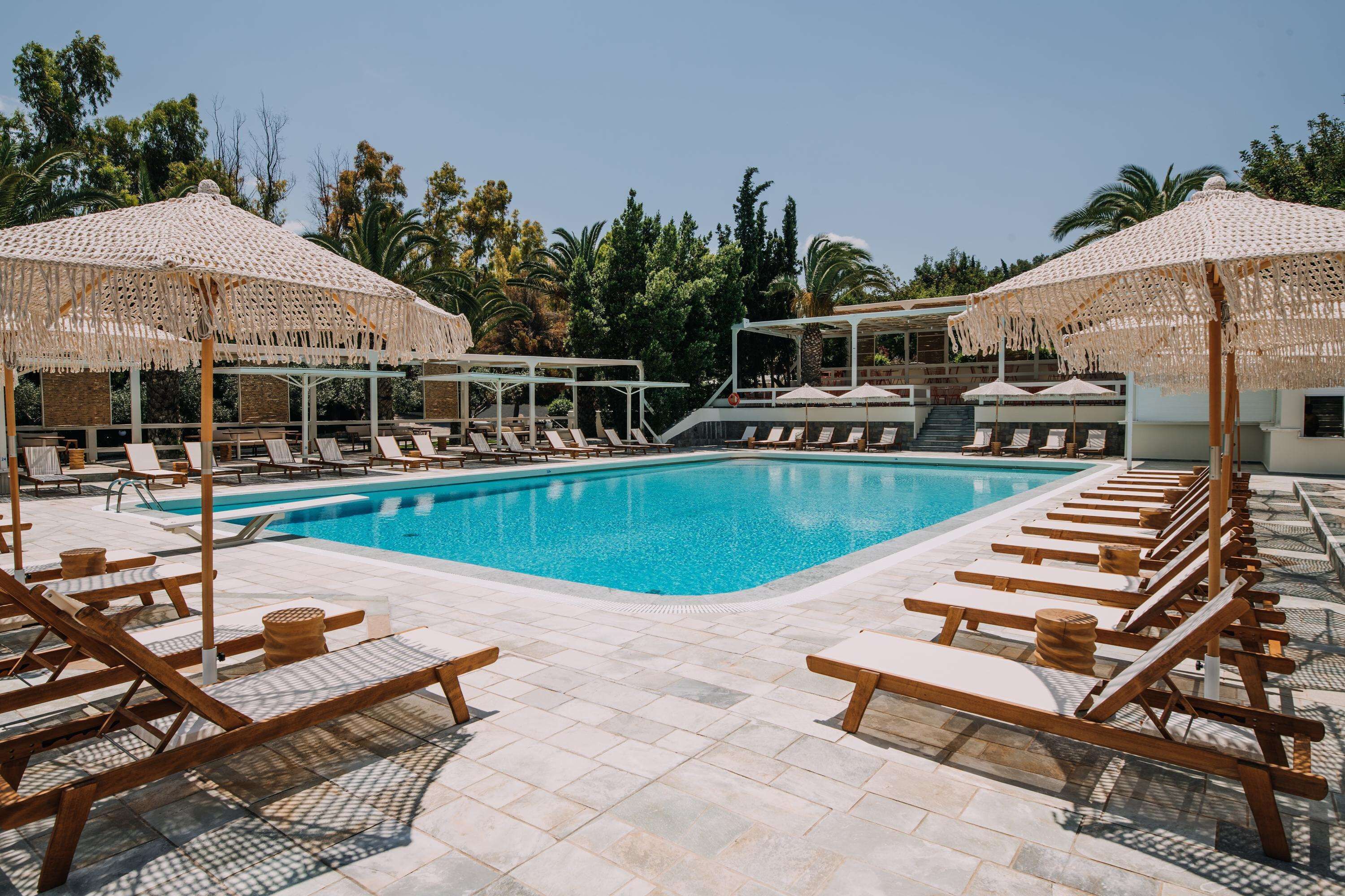A pool area with wooden loungers and thatched umbrellas, surrounded by palm trees.