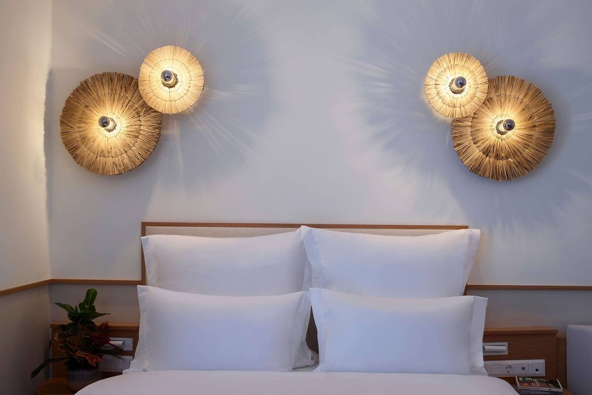 A hotel room with a bed, two wall-mounted lamps, a nightstand with a plant, and a bedside table with a book.