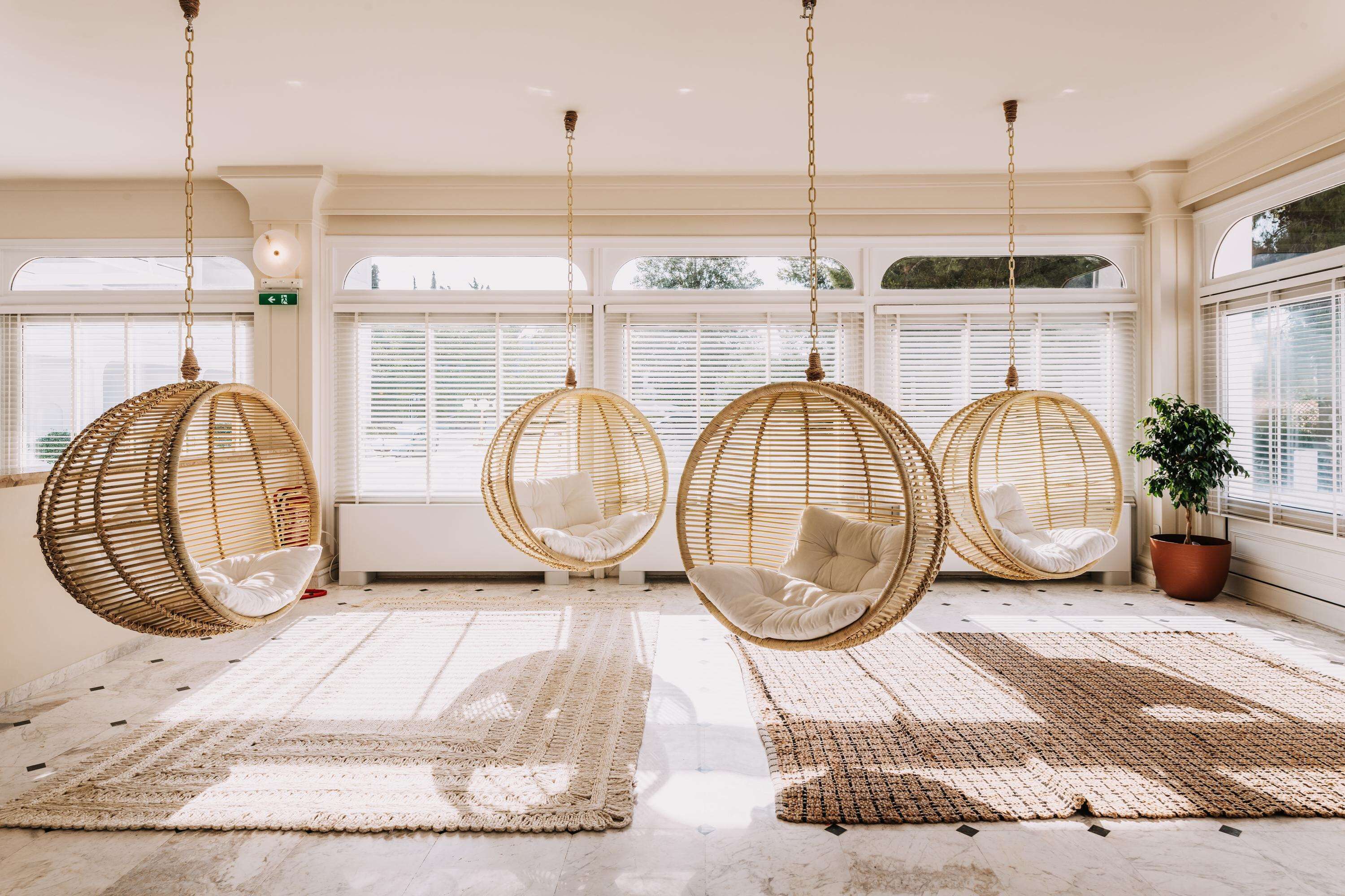 Une pièce avec quatre chaises en osier suspendues, un grand tapis tissé et une plante en pot près de la fenêtre.