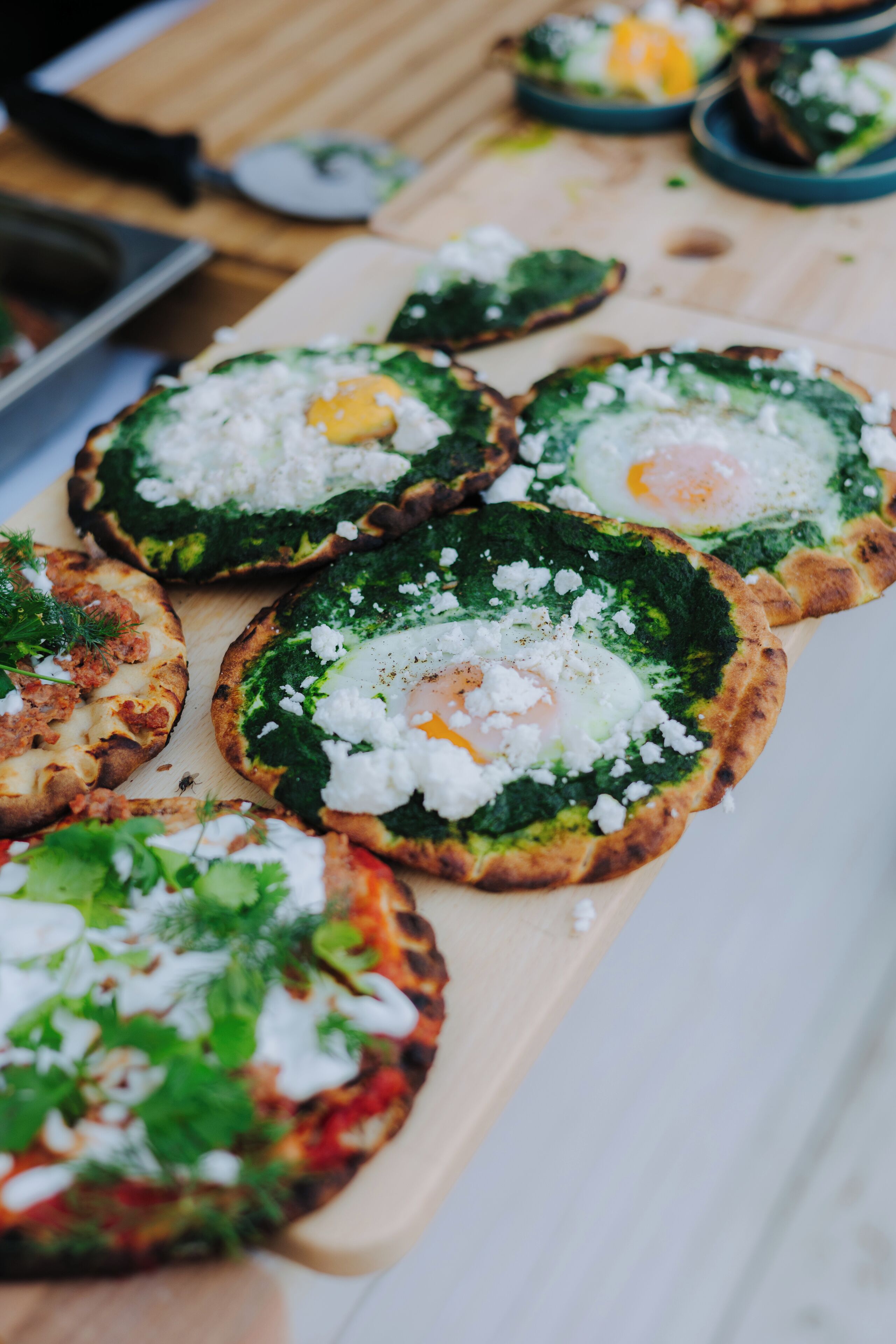 A wooden board with several small, round, baked dishes topped with greens, cheese, and eggs.