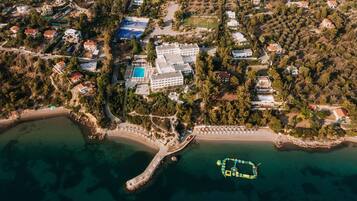 An aerial view of a coastal resort with a central building surrounded by villas, a beach, and a pier.