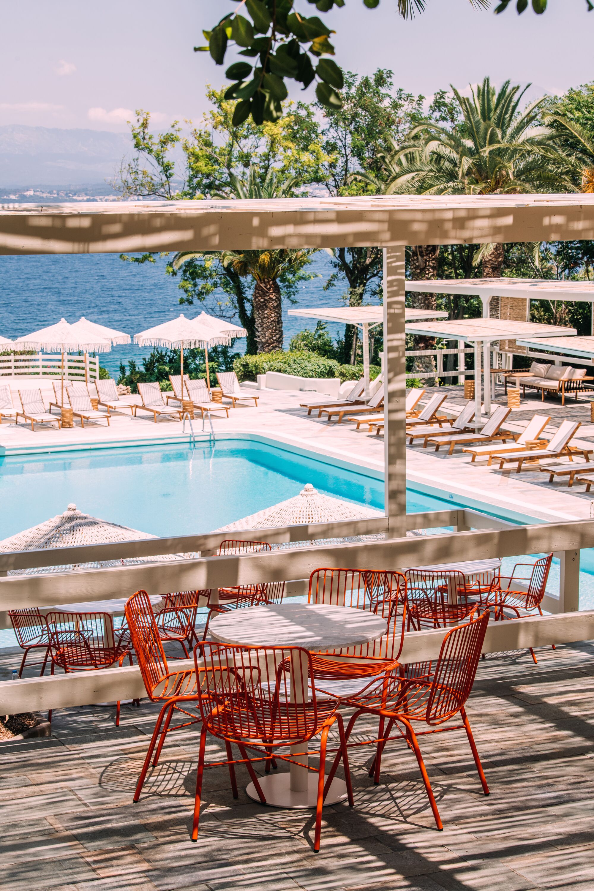 A poolside area with lounge chairs and umbrellas, a pool, and a view of the sea.