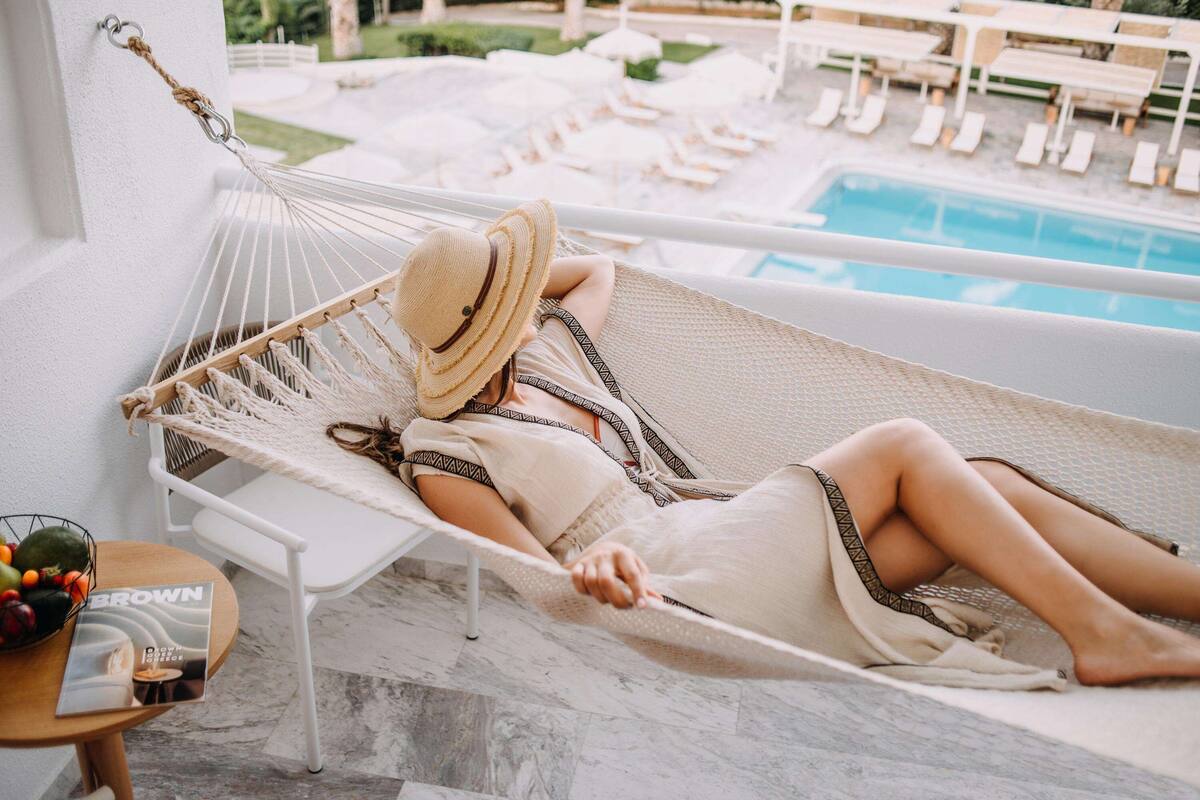 A person relaxing in a hammock by a poolside, with lounge chairs and a swimming pool in the background.