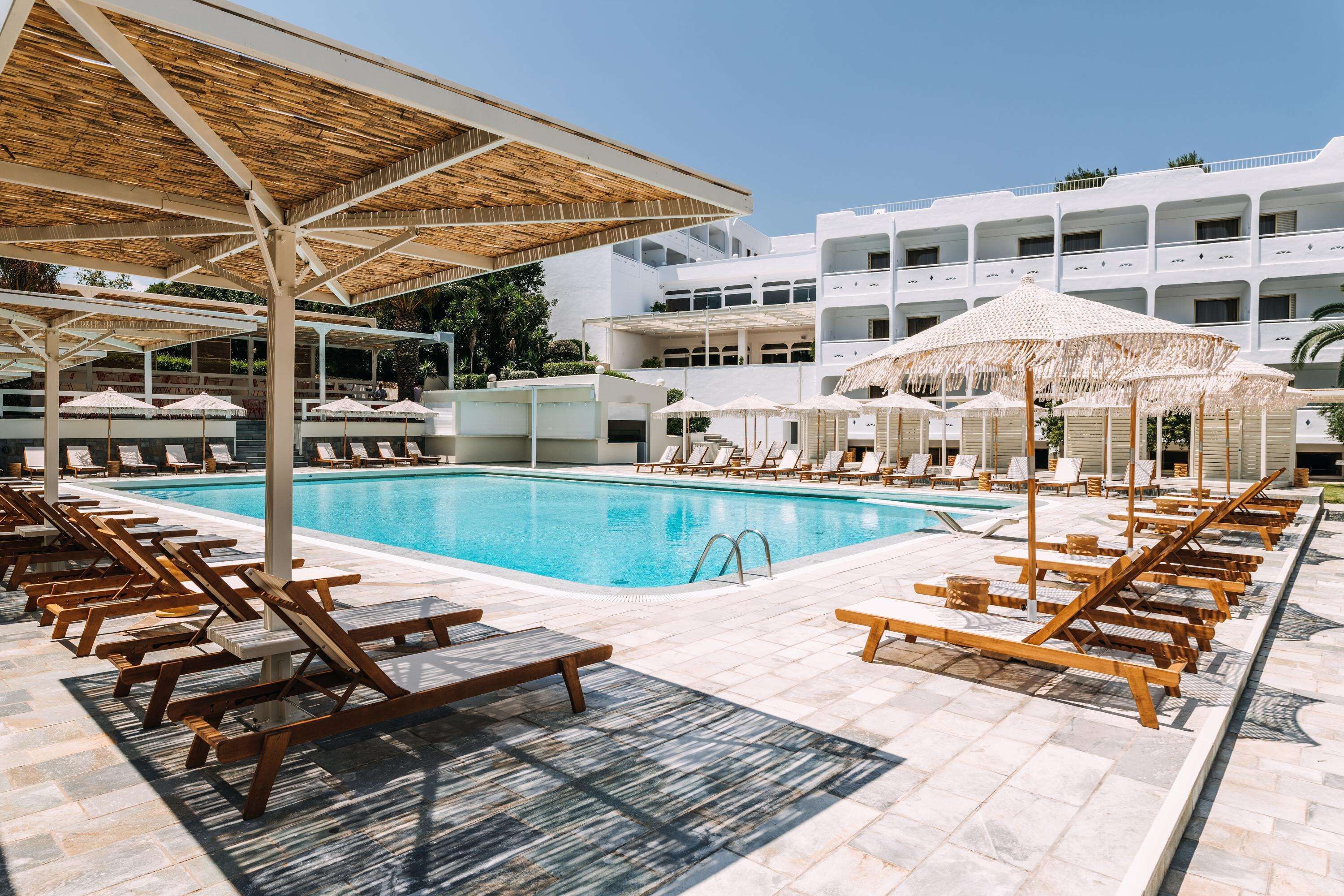 A poolside area with sun loungers and umbrellas, a clear blue pool, and a modern building in the background.