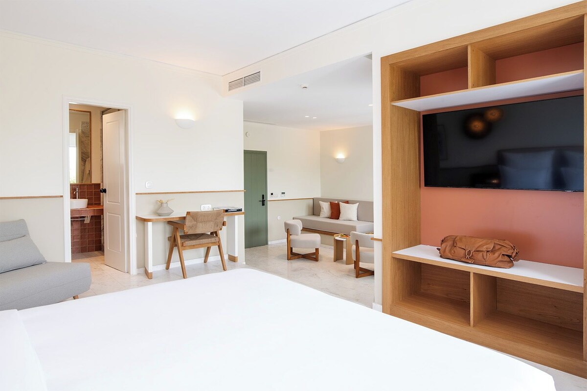 A modern hotel room with a bed, a desk, a chair, a sofa, a TV, and a wardrobe.