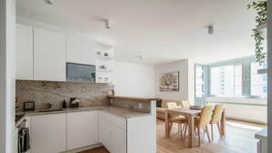 A modern kitchen with white cabinets, a marble countertop, and a dining area with a wooden table and chairs.