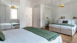 A modern bedroom with a large bed, a smaller bed, and a walk-in closet with mirrors.