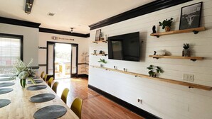 A modern dining area with a long wooden table, multiple chairs, and a TV mounted on the wall. - ⛱  Spacious, Private Pool, Golf Cart - just RELAX  🏝 (Panama City Beach)