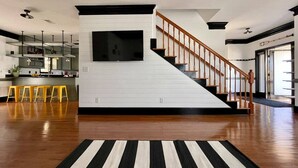 A modern living room with a wooden staircase, a flat-screen TV mounted on the wall, and a striped rug on the floor. - ⛱  Spacious, Private Pool, Golf Cart - just RELAX  🏝 (Panama City Beach)
