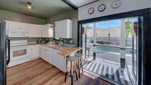 A modern kitchen with white cabinets, a wooden countertop, and a built-in oven. There is a bar stool and a view of a swimming pool through a glass door. - ⛱  Spacious, Private Pool, Golf Cart - just RELAX  🏝 (Panama City Beach)